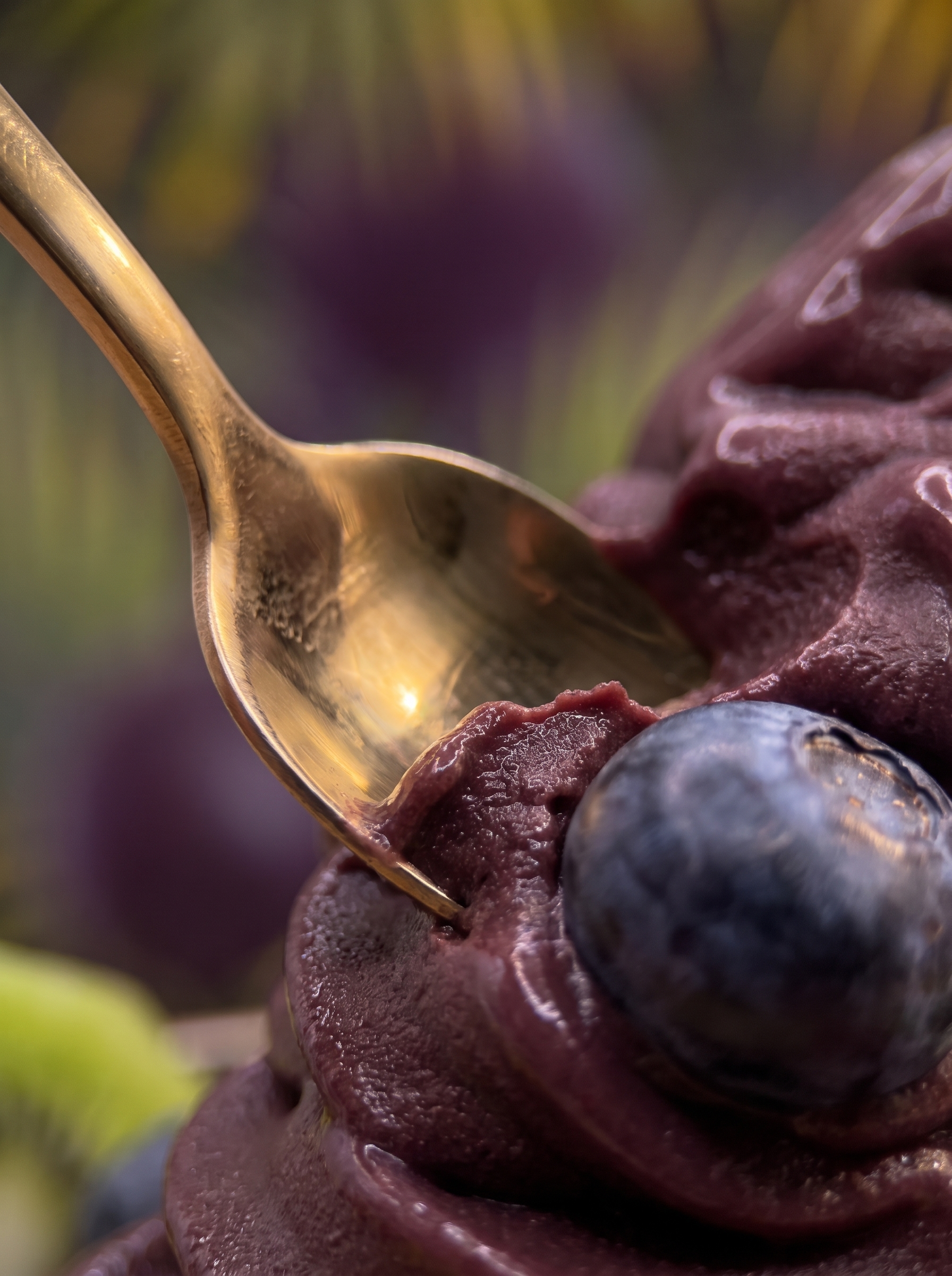 Close-up of Savor açaí, showing the deep purple creamy texture with a golden spoon and a fresh blueberry.